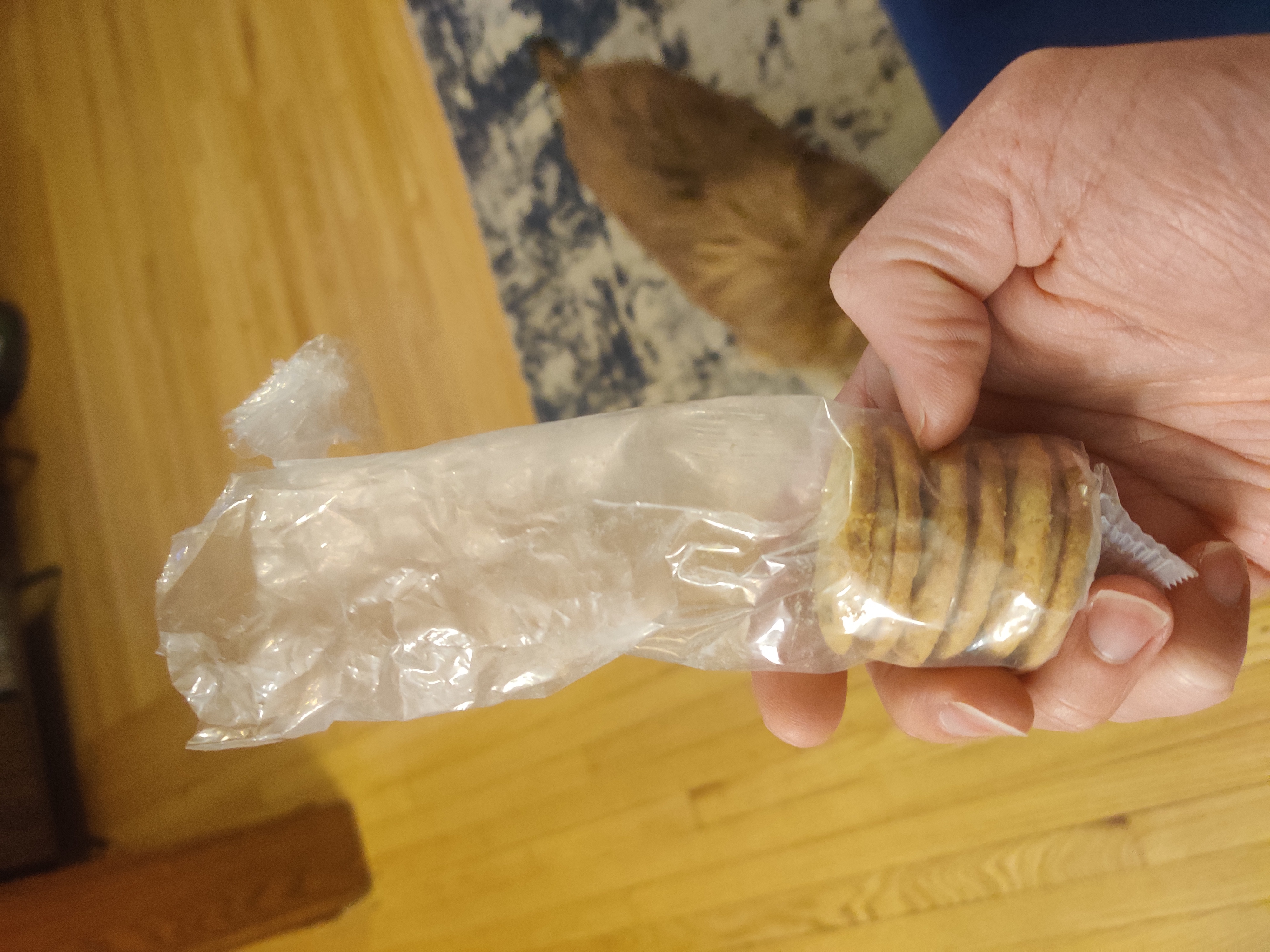 Three peanut butter sandwich cookies left in a plastic sleeve. A wood floor and a small brown dog are in the background.