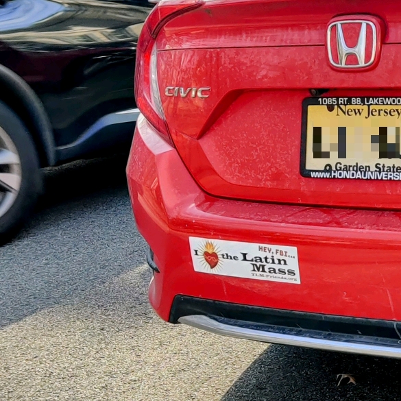 A bumper sticker, on a red Honda Civic with a New Jersey license plate, that reads "Hey, FBI… I ❤️ the Latin Mass / TLM-friends.org".