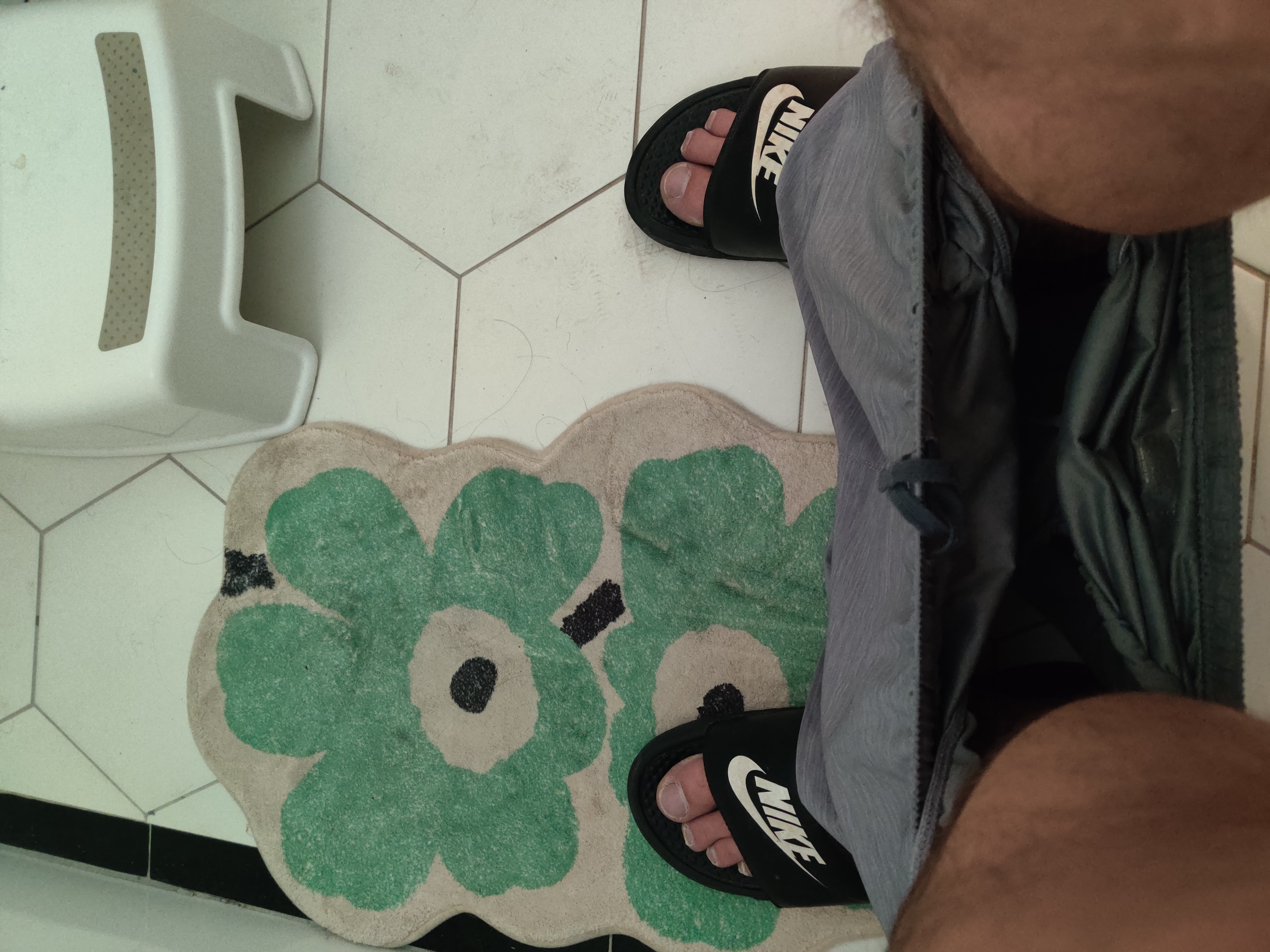 POV: you're pooping on company time, staring at your feet and a bath mat on a white, hexagonal tiled floor.